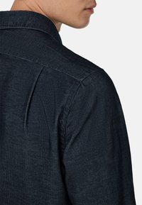 Camicia button-up di un blu scuro con tessuto testurizzato, colletto a punta e sottili motivi a righe verticali sulla schiena e sulle maniche.