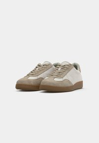 Beige en witte sneakers met een bovenwerk van suède en leer, ronde neus, platte vetersluiting en rubberen zool. Minimalistische stijl met tonale accenten.