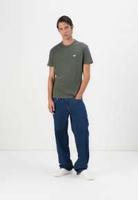 Tricou din bumbac verde măsliniu cu decolteu rotund și mâneci scurte, asortat cu blugi largi albaștri și adidași albi.