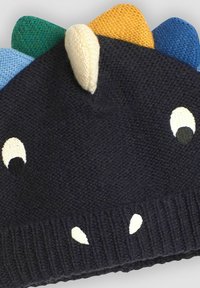 Gebreide beanie in donker marineblauw met gekleurde spikes in blauw, groen, geel en crème. Heeft cartoonogen en tanden in contrasterend wit en zwart.