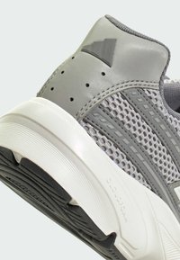 Gros plan sur le talon d'une chaussure de sport grise avec tissu en maille, empiècements synthétiques, trous de ventilation, semelle blanche rembourrée et motif de semelle noir.