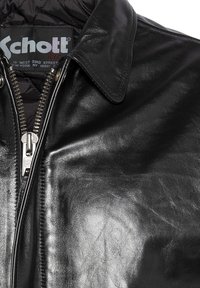 Veste en cuir noir avec fermeture éclair, col pointu et intérieur matelassé. Le matériau présente une finition lisse et brillante avec des coutures visibles.