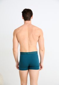 Τεάλ κοντές κάλτσες ανδρικές με σκούρο λάστιχο που φέρει τη γραφή "BJÖRN BORG". Το ύφασμα είναι λείο με εφαρμοστή γραμμή και ελάχιστες ραφές.