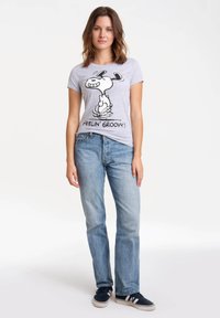 T-shirt gris avec un personnage de bande dessinée et le texte "FEELIN' GROOVY!" assorti à un jean bleu clair et des baskets noires.