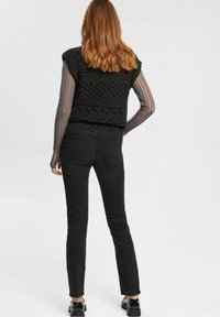 Top negro de punto sin mangas con diseño de trenzado texturizado, combinado con jeans negros ajustados. Blusa de manga larga transparente superpuesta.