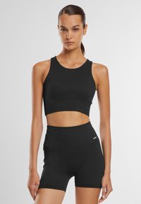 Top court noir à côtes et short taille haute. Tissu extensible, design sans manches, couture minimale et détail du logo sur le short.