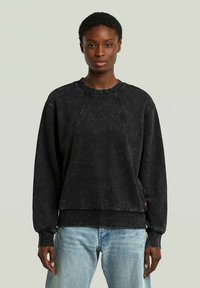 Felpa nera con una vestibilità comoda, maniche raglan, cuciture visibili e una texture morbida. Abbinata a jeans in denim azzurro chiaro.