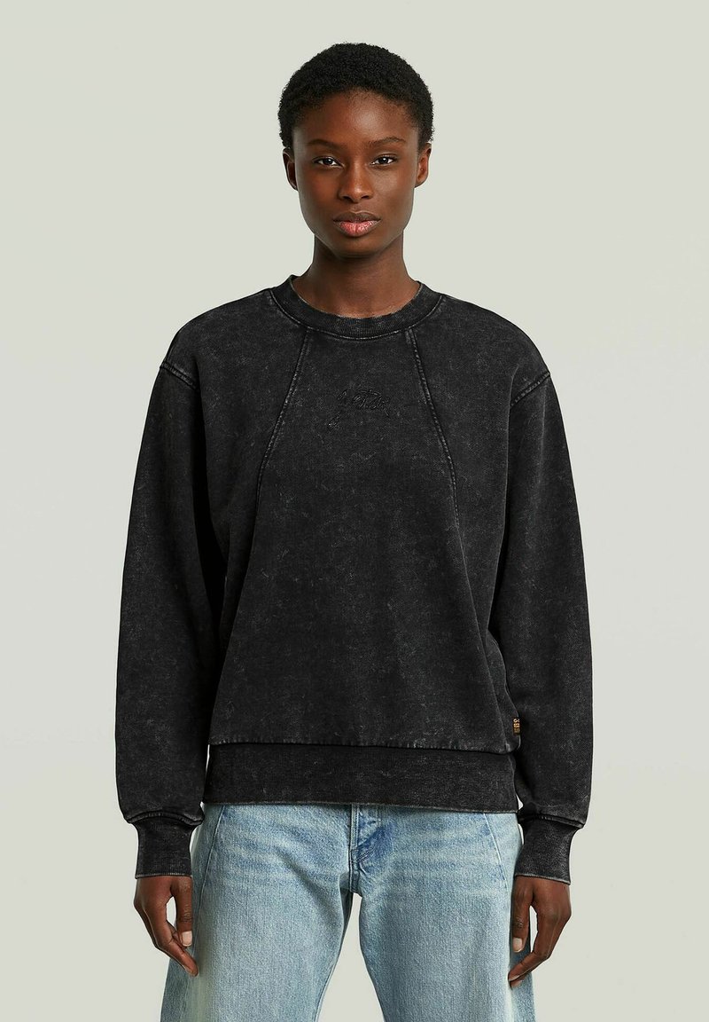 Felpa nera con una vestibilità comoda, maniche raglan, cuciture visibili e una texture morbida. Abbinata a jeans in denim azzurro chiaro.