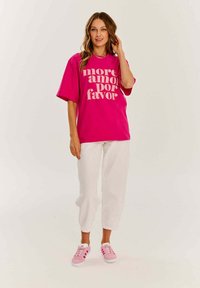 Růžové oversized tričko s bílým nápisem "more amor por favor", doplněné bílými culotovými kalhotami a růžovými teniskami.