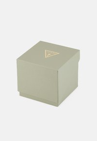 Kvadratinė šviesiai žalia dėžutė su tekstūruota paviršiumi ir auksiniu trikampio logotipu viršuje. Uždaryta ir pasižyminti paprastu dizainu.