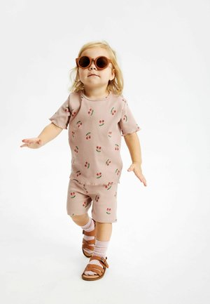 Conjunto de color rosa con relieve, de mangas cortas y pantalones cortos, con un estampado floral. Unas gafas de sol marrones y sandalias marrones completan el conjunto.