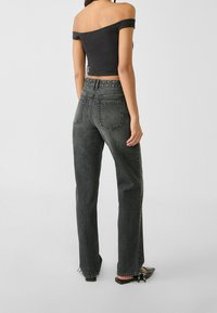 Donna vista di spalle che indossa un top nero off-shoulder, jeans grigi scuri a vita alta e ballerine nere a punta.