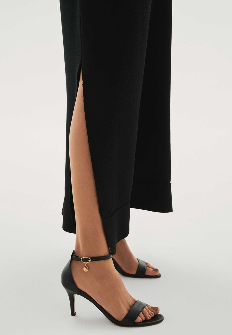 Mustast pahkluu pikkusest kleidist, millel on küljes mõlemal k�üljel lõhikud, kombineeritud mustade kõrge kontsaga sandaalidega, millel on peen rihm ja pahkluu rihmal kuldne ripats.