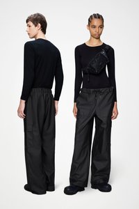 Μαύρα μακρυμάνικα τοπ συνδυασμένα με άνετα, μαύρα cargo παντελόνια με ελαστικές μέση και πολλές τσέπες. Μία μοντέλο κρατάει μια τσάντα με υφή.