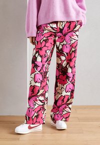 Blommönstrade vida byxor i livliga nyanser av pink, röd och beige, kombinerade med vita sneakers och en rosa tröja. Slät tygtextur.