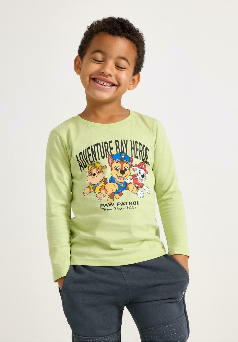 Lichtgroen T-shirt met lange mouwen en een grafische afbeelding van drie cartoonhonden. Gecombineerd met donkergrijze broek met zakken en een gestructureerd oppervlak.