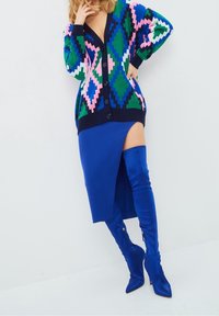 Colorful knitted cardigan with diamond patterns in pink, green, and blue; paired with a blue knee-length skirt and blue thigh-high boots.