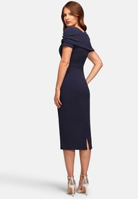 Marineblaues, tailliertes Kleid mit schulterfreiem Design, in mittellanger Länge, aus strukturiertem Stoff und mit einem Schlitz an der Seite, kombiniert mit metallischen Absätzen.