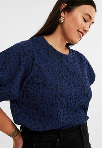 Marinbl å strukturerad topp med leopardmönster, korta ärmar och rund halsringning, matchad med svarta byxor.