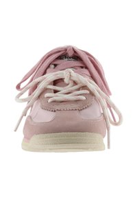 Vista frontal de una zapatilla deportiva de color rosa claro con cordones blancos y rosas atados en un nudo sobre la lengüeta y suela beige.