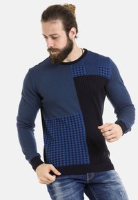 Blauer Langarm-Pullover mit strukturierten Einsätzen, ausgestattet mit Rips- und Hahnentrittmustern. Klassischer Rundhalsausschnitt und eng anliegende Bündchen.
