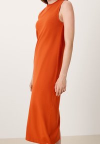 Pomarańczowa sukienka do kostek, bez rękawów, z wysokim dekoltem, gładka w dotyku, minimalistyczny design, z delikatnym rozcięciem po boku i detalem logo.