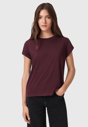 T-shirt bordeaux a maniche corte in morbido cotone, con collo a giro e orli arrotolati, abbinato a jeans scuri.