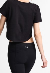 Musta lyhythihainen crop-top, valmistettu sileästä kankaasta. Yhdistetty mustiin korkeavyötäröisiin legginsseihin, joissa on logo vyötärönauhan kohdalla.