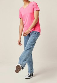 Lyserød kortærmet V-hals T-shirt parret med lyseblå denimjeans og sorte lavtoppede sneakers. Enkel design med en afslappet pasform.