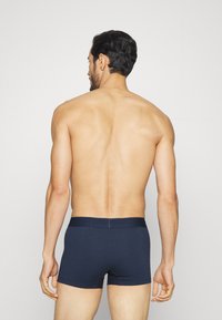 Boxers-briefs bleu marine avec une taille élastique, texture lisse et design ajusté, présentés de l'arrière sur un torse nu.