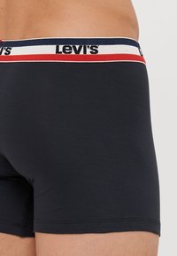 Fekete pamut boxer alsók, kontrasztos derékrésszel, piros és tengerészkék csíkokkal, valamint "Levi's" márkázással. Puha tapintású és testhezálló fazon.