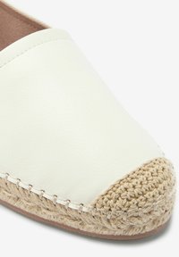Valkoinen nahkainen espadrille, jossa on kudottu juutti-kärkiosuus. Varustettu ommellulla reunalla ja sileällä pintarakenteella. Yksinkertainen muotoilu, joka antaa rentoa ilmettä.