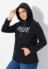 Zwarte hoodie met "TRUE" in zilver gedrukt. Voorzien van een trekkoord met zwart-wit patroon, zijzakken en zijsplitten.