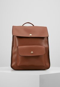 Ruskea nahkainen reppu, jossa on tasainen yläluukku ja etutasku. Varustettu kulta-värisellä painonapilla ja minimalistisella designilla. Sileä pinta.