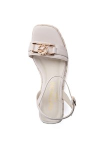 Sandal de color gris claro con suela plana, detalle de yute trenzado y hebilla en tono dorado en la correa. Diseño simple, textura suave.