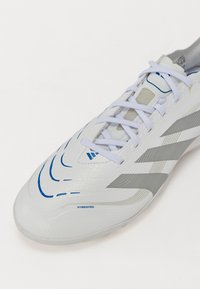 Weißer Sportschuh mit einer glatten, strukturierten Oberfläche, der blaue und silberne Akzente aufweist, eine abgerundete Zehenpartie hat und weiße Schnürsenkel besitzt. "HYBRIDFEEL" ist eingeprägt.