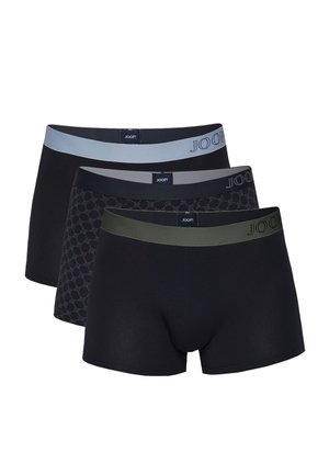 Fit erwachsener Mann steht barfuß vor einfachem Hintergrund, trägt schwarze Boxershorts mit grauem Bund.