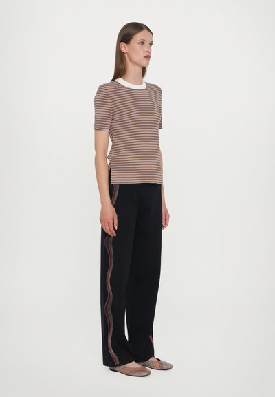 Gestreept T-shirt in bruin, oranje en blauw met witte kraag; zwarte broek met golvende rode en witte zijkanten; gestreepte instap schoenen.
