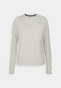 T-shirt de sport à manches longues gris clair en tissu lisse. Présente un col rond et un petit logo blanc sur le haut à gauche de la poitrine.