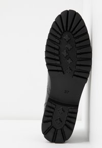 Semelle de chaussure noire avec des rainures profondes, motifs en forme de croix au centre, et numéro de taille 37 imprimé près du talon.