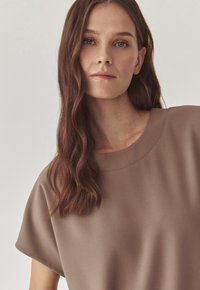 Brown, short-sleeved top made of soft fabric with a round neckline and smooth texture, featuring a slightly oversized fit.