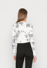 Top cropped de manga longa em branco com um padrão de tie-dye em preto, apresentando um decote redondo e mangas ajustadas. Combinado com calças pretas de cintura alta.