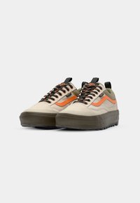 Zapatillas de lona beige y oliva con acentos naranjas, cordones negros y suela de goma texturizada. Cuenta con una pestaña en el talón.