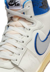 Højtop hvid Nike Air sneaker med blå accenter, hvide snørebånd, tekstureret læder og synligt swoosh-logo på siden.