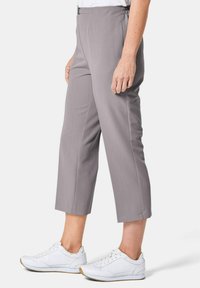Graue, cropped Hosen mit glatter Textur, ausgestattet mit einem elastischen Bund und zwei seitlichen Taschen. Kombiniert mit weißen Sportschuhen.