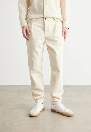 Pantalones de pana color crema con un corte relajado, que cuentan con bolsillos laterales y un cierre de un botón. Combinados con zapatillas blancas.