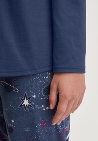 Donkerblauw shirt met lange mouwen van een gladde stof, gecombineerd met gestreepte leggings met sterren, planeten en kleurrijke kosmische ontwerpen.