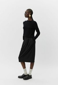 Czarny dzianinowy sweter z okrągłym dekoltem, zestawiony z czarną plisowaną spódnicą do kolan. Dodatki to złote kolczyki-koła i okulary przeciwsłoneczne.