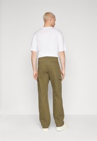 Olivgrüne Cargo-Hosen mit Seitentaschen, lockerer Passform und glatter Textur, kombiniert mit einem schlichten weißen T-Shirt. Stehende Ansicht von hinten.