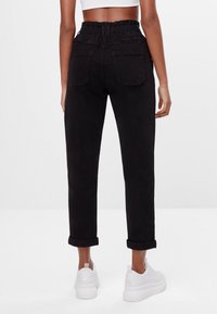 Pantalones negros ajustados con una cintura alta elástica, puños enrollados y dos bolsillos traseros, combinados con zapatillas deportivas blancas. Tela de algodón suave.